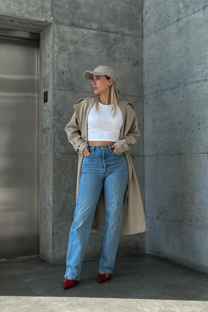 White crop top, light wash high-waisted jeans, beige trench coat, and red kitten heels